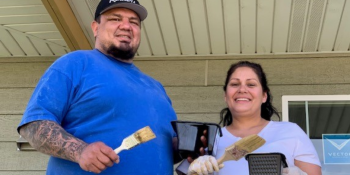 A man and a woman smiling at camera as they paint.