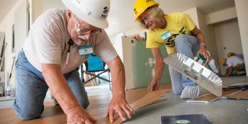 Two RV Care-A-Vanner volunteers lay down flooring.