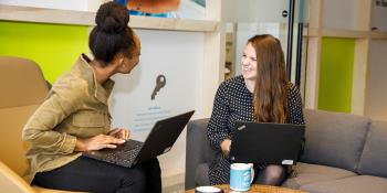 Two young professionals sit in chairs in a bright colored office.