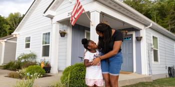 Mother and daughter smiling at each other while standing in front of house