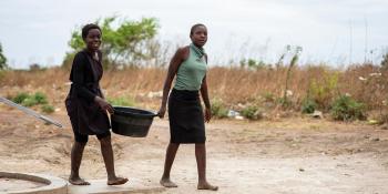 Two Zambian women carry a bucket of clean water between them.