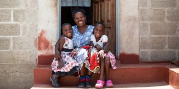 A Zambian woman hugs her two daughters on the front step of their brick home.
