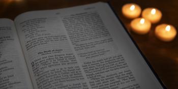 An open Bible with lit candles in the background.
