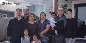 Large family of 9 standing together in front of Habitat home.