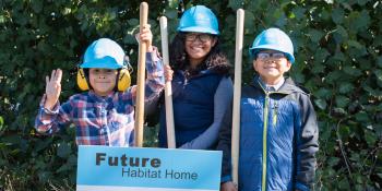 Three kids in Habitat hard hats next to a sign reading "Future Habitat home"