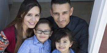 family of four sitting in the doorframe of their home together smiling.