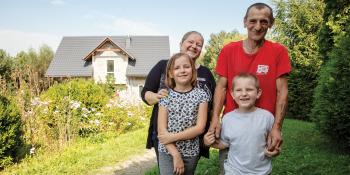 family of four standing in their flower garden in front of their home.