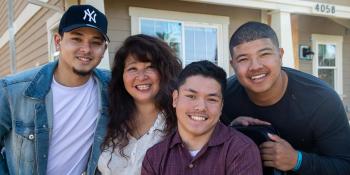 Mother with three young adult sons smiling together in front of their home.