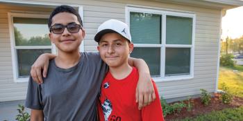 Two adolescent brothers smiling together in front of their home.