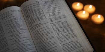 An open Bible in Spanish with lit candles in the background.