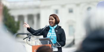 Woman in a blue Habitat scarf speaking at a podium at a rally in Washington, D.C.