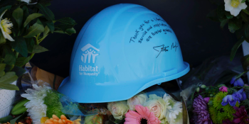 Laying on a bed of flowers is a light blue hardhat with the Habitat logo and a message written on the side that reads "Thank you for a lifetime of service and inspiration. We are forever grateful" signed by Habitat CEO Jonathan Reckford.