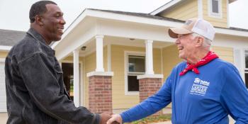President Carter in red bandana and blue Habitat shirt shaking hands with man in front of Habitat house