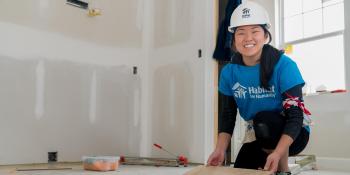 Young woman collegiate challenge volunteer smiles while working inside an unfinished house.