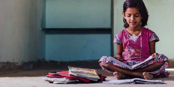 young girl in India reading on her concrete floor.