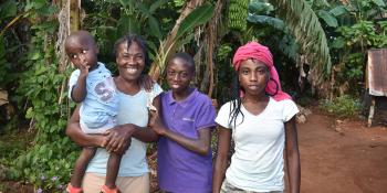 Princile with three of her children standing among lush tropical foliage.