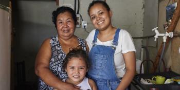 Woman smiling with her adult daughter and young granddaughter in their home in Brazil.