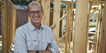 portrait of Habitat CEO Jonathan Reckford smiling standing in house framing on build site.