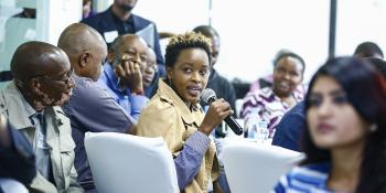 Woman speaking into a microphone in a crowd at ShelterTech Kenya event.