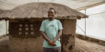 Jacob Simwero, a staff from the Terwilliger Center Shelter Venture Lab postures outside a model hut at Kenya Medical Research Institute