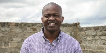 Kenyan man standing smiling in front of brick wall.