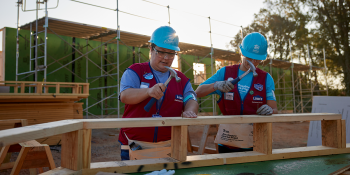 Two Lowe's employees in hard hats and red vests hammer on Carter Work Project 2023 build site.