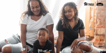 A mom sits with her daughter and young son on the floor of their home.