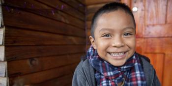 Mexican boy in scarf smiling in front of his home