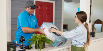 Man volunteering as a Habitat ReStore cashier wearing ReStore branded shirt and hat and helping woman buying items.