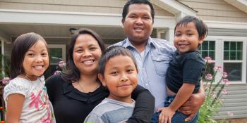 family of five smiling in front of house.