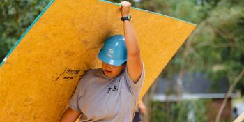 Woman volunteer in hard hat carrying a sheet of plywood 