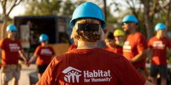 Group of volunteers wearing red Habitat shirts hold hands in a circle to pray