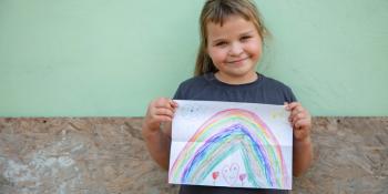 Little girl holds a drawing of a rainbow.