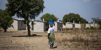 Margaret carries water from the nearby access point to her home in Zambia built by Habitat Zambia, which feature concrete block construction and securely fastened roofs. 