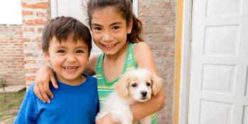 Two children smiling with puppy in front of house