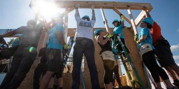 A group of volunteers raising a framed wall as the sun shines behind them.