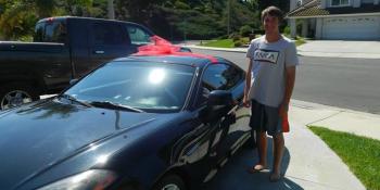 Black car with a red bow and a teenage boy standing next to it.