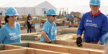 Jonathan Reckford and two volunteers carry wooden house framing on the site of the 2025 Carter Work Project.