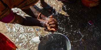 Overhead view of woman washing hands over a bucket of sudsy water.