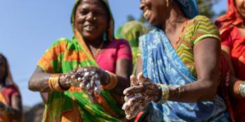 Two women in colorful saris washing their hands.