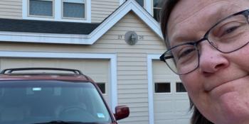 Red Acura with a woman in a purple and blue striped shirt and glasses standing in front of it.