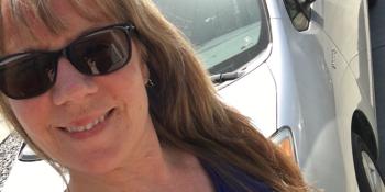 Woman in a blue shirt and sunglasses in front of a silver Prius.