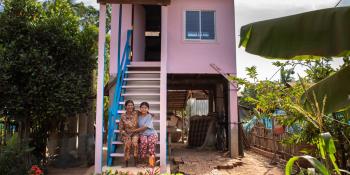 Mother and daughter sitting on steps of their pink and blue house.
