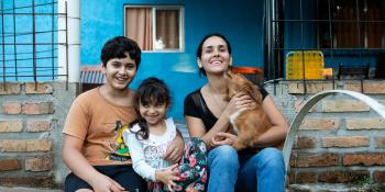 Woman sitting in front of her blue house with her two children and dog.