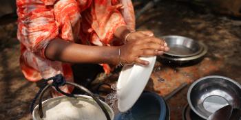 Person in orange garment crouched down and washing dishes at the community well.