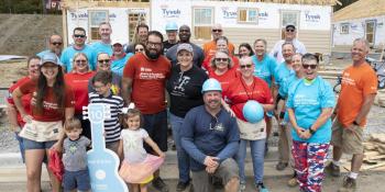 Group of smiling volunteers in front of framed house on build site