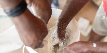 Multiple hands reach into a bucket to help mix a building material.