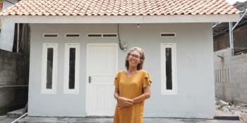 A woman in an orange dress stands in front of her home.
