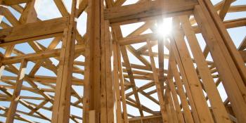 Sun shining through roof trusses of wood house frame.
