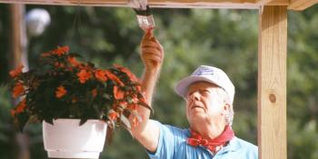 President Carter painting a porch roof, wearing a cap and red bandana.